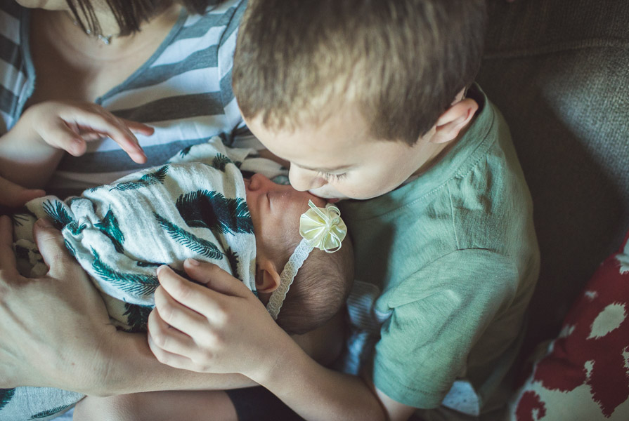 brother kissing newborn baby sister on forehead, overhead shot