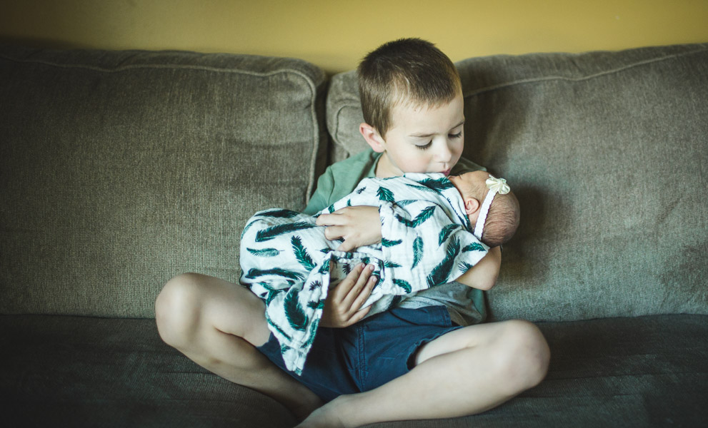 brother snuggling with baby sister on couch 