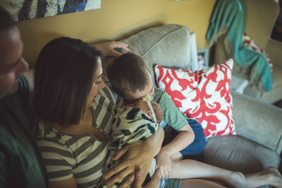 brother nuzzles his forehead against baby sisters' in mother's loving arms