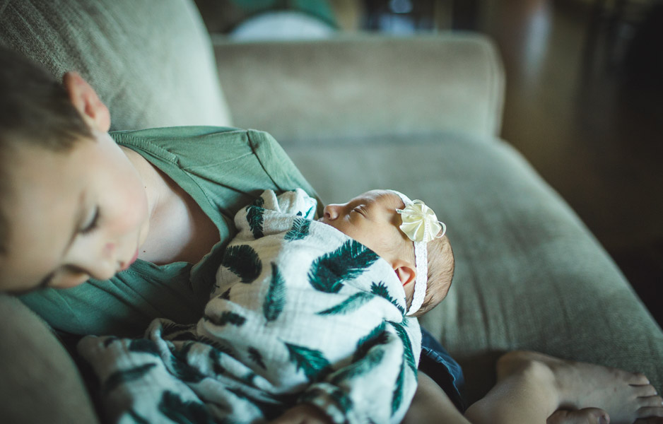 tender moments of brother resting with newborn baby sister on couch 