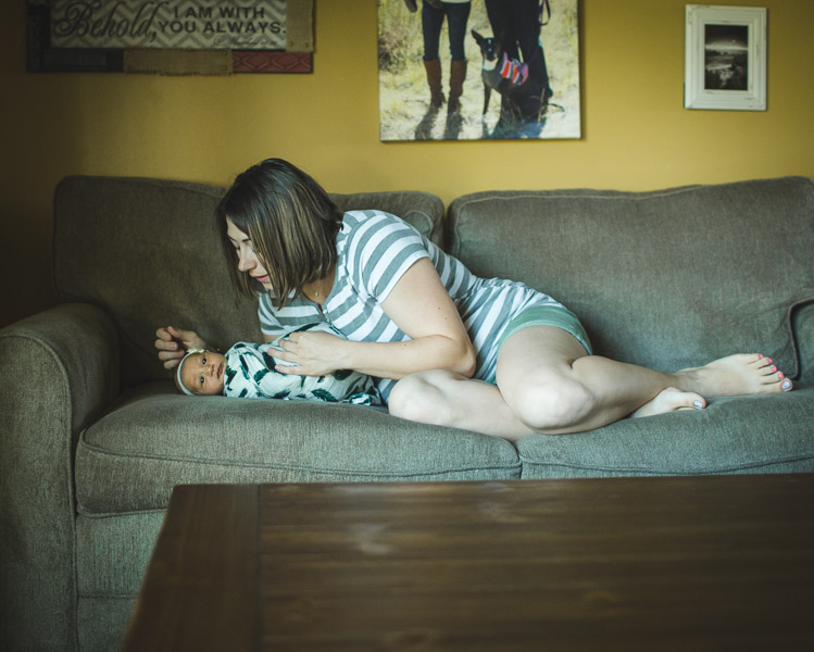 mother admiring newborn child on couch in soft window light