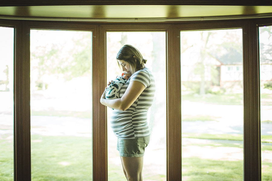 portrait of mother with newborn cradled into her in front of bay windows