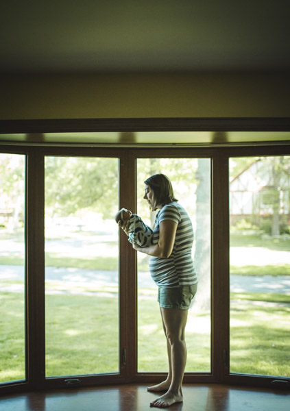 portrait of mother cradling newborn daughter in front of bay windows