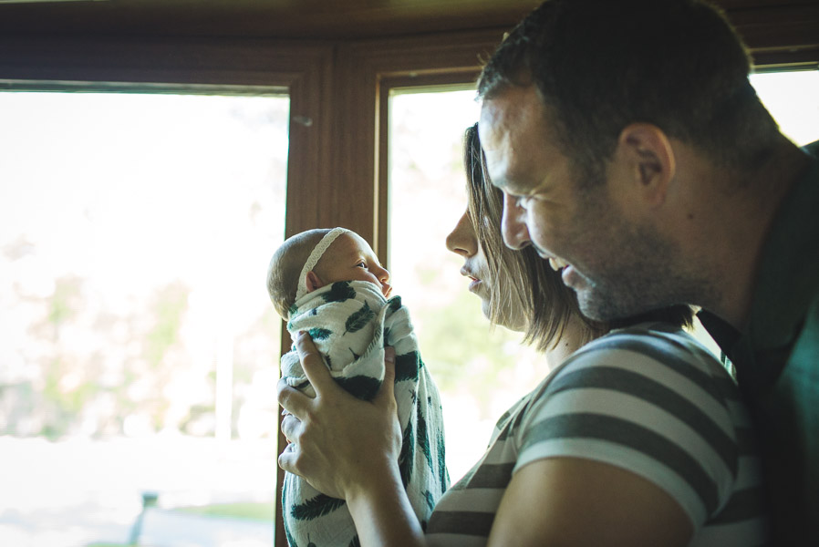 father smiling on newborn daughter over mother's shoulder as she holds her close