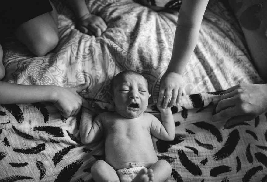 documentary, newborn child holding hands with siblings, overhead portrait; black and white