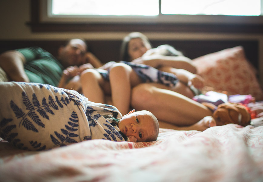 portrait of newborn child in focus with family snuggles behind 