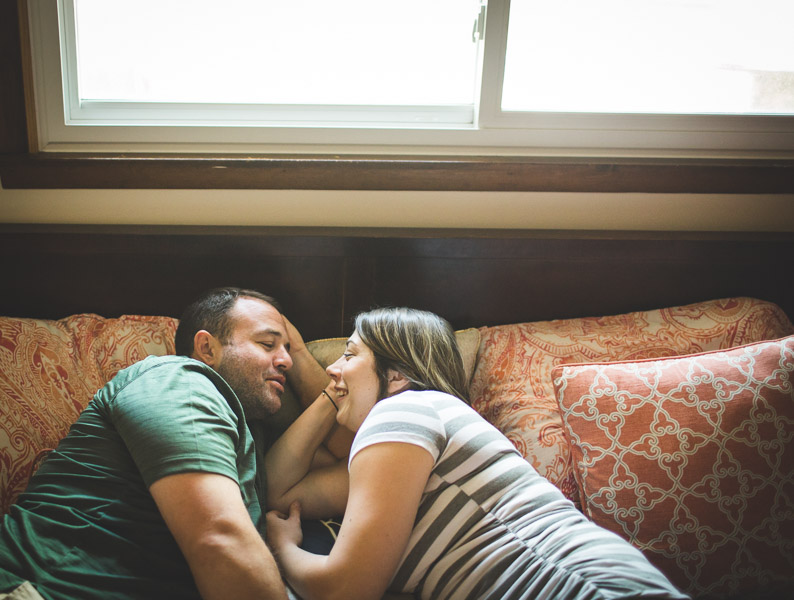 couples snuggling on bed in soft window light 