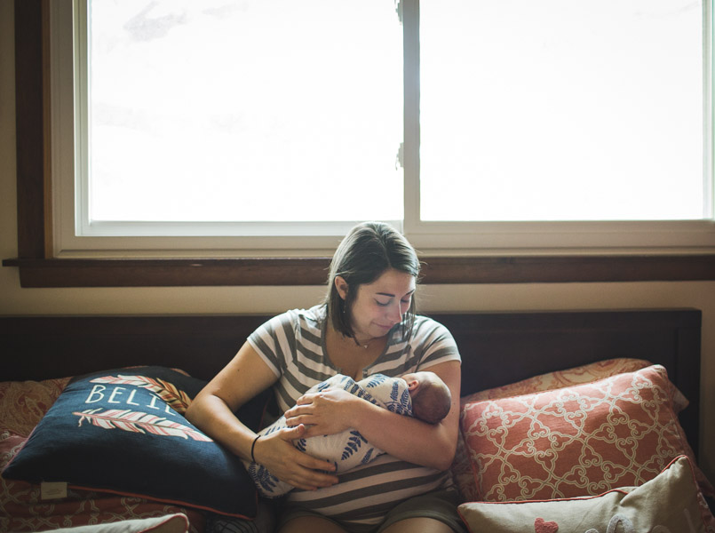 Mother cradling infant in front of large window on bed 