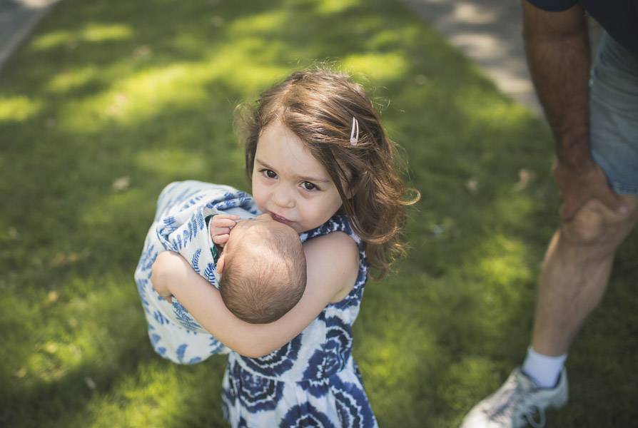 sister carrying newborn baby across yard, movement, powerful, connection