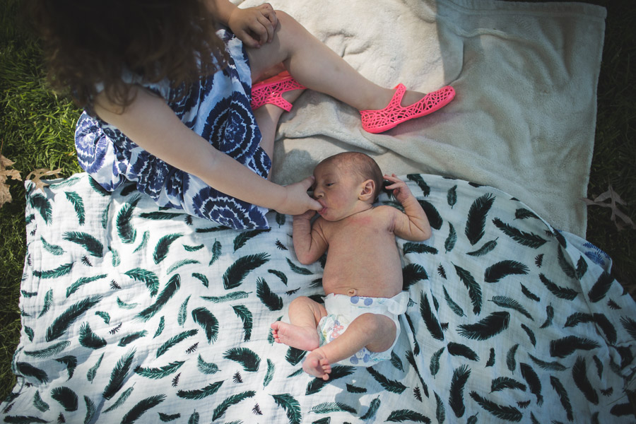 sister holding baby sisters hand on blanket outside in morning light