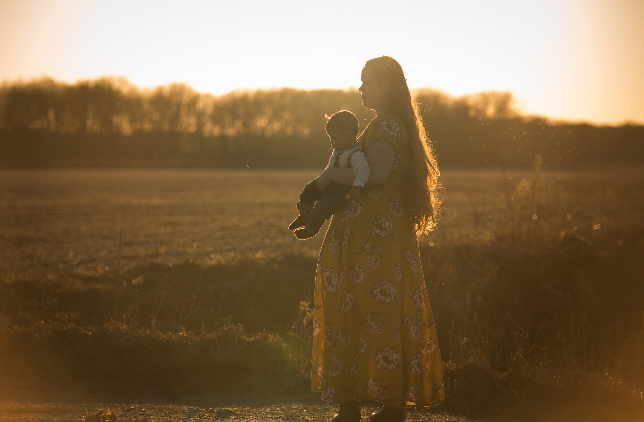 Mother walking in the field carrying her son in the golden sunset