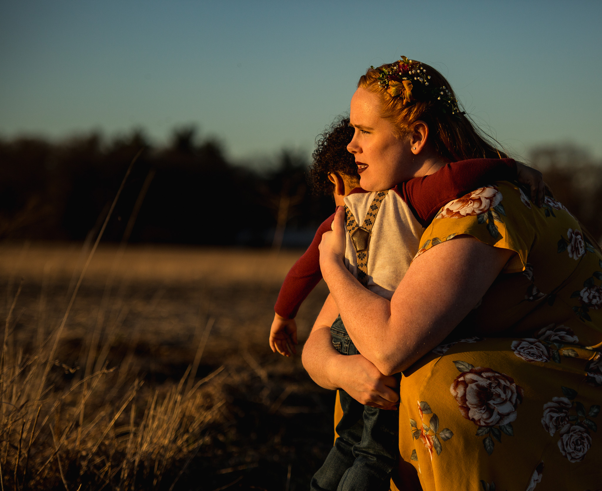 Mothering lovingly hugging her son in wide open field during golden sunset