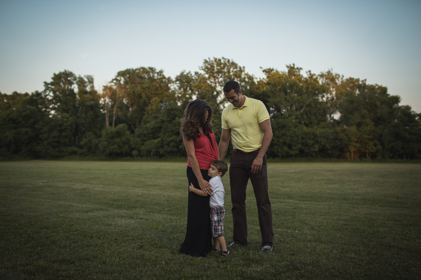 Little boy hugging mothers leg with father admiring beside in wide open field at Coffee Creek Watershed Preserve, Sunset