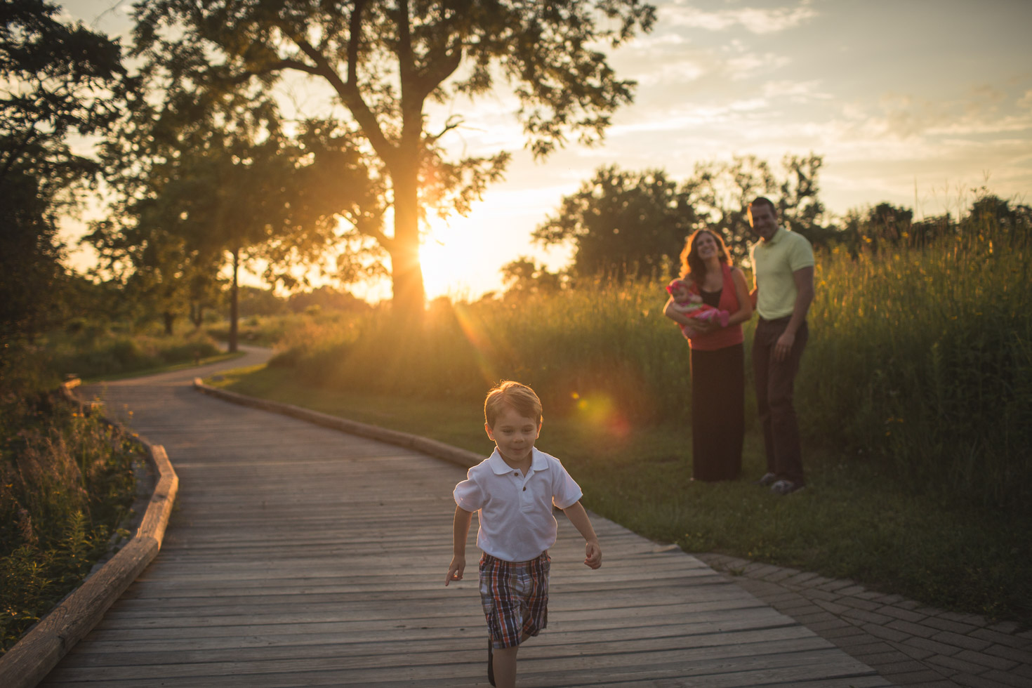 Boy running through golden light with family watching from behind, Coffee Creek Watershed Preserve