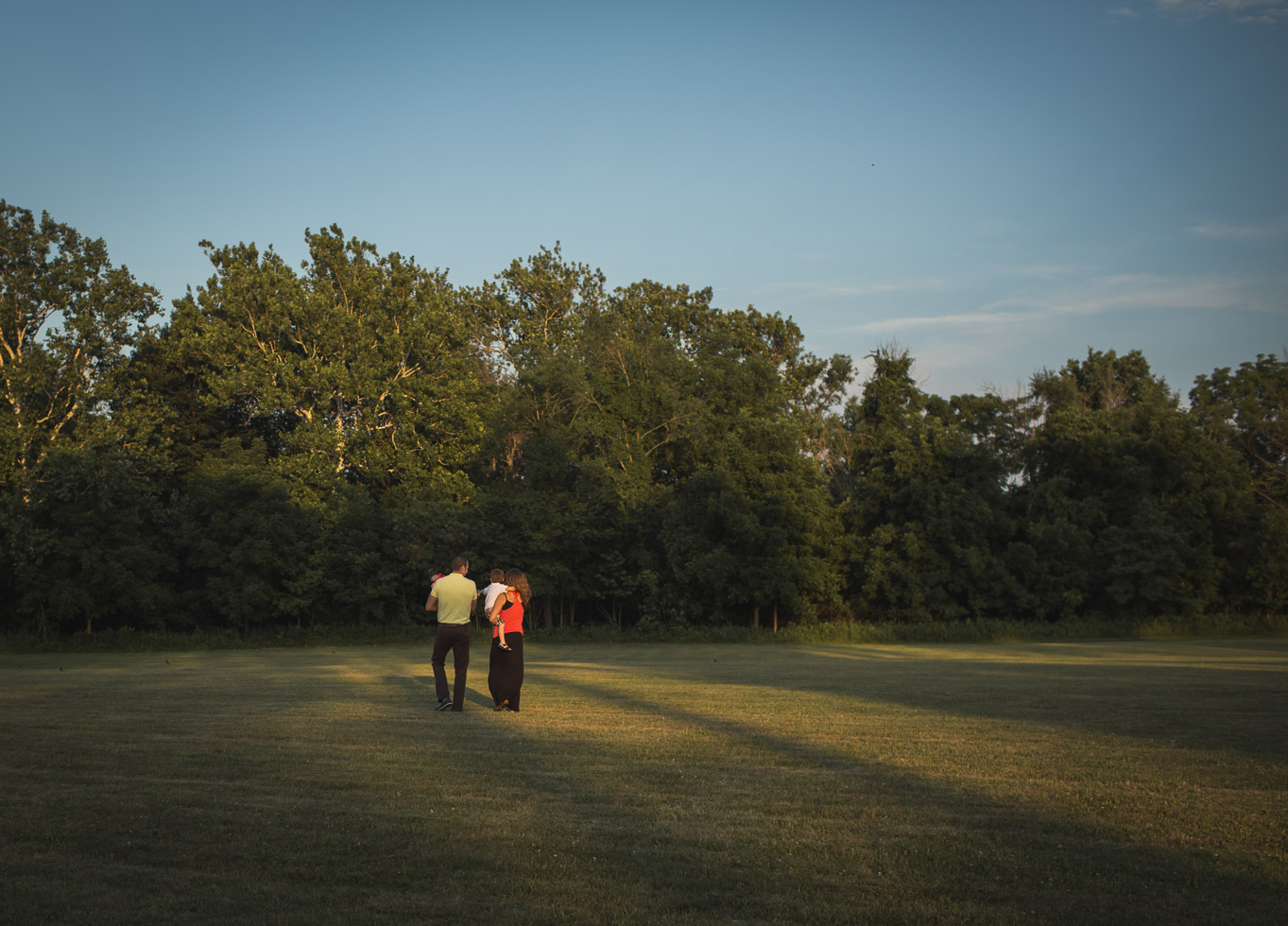 Family walking together in golden evening light in wide open field 