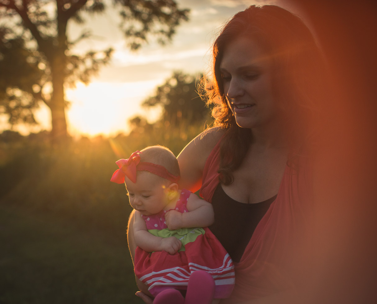 Mother holding child in warm sunlight with lens flare, backlight