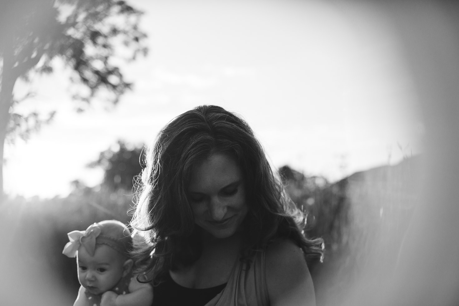 Mother embracing her child in love, as she looks down in gratitude, backlight, lens flare, bokeh, black and white, emotional motherhood portrait 