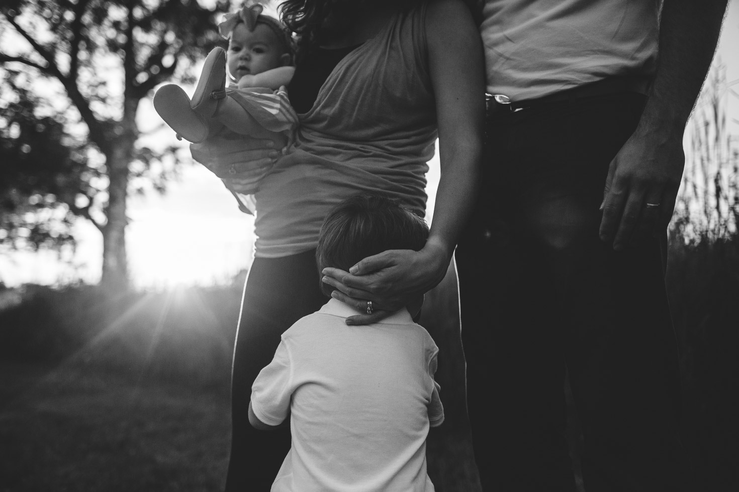 Emotional Family portrait as mother embraces sons head as she holds her daughter, backlight, black and white, documentary style 