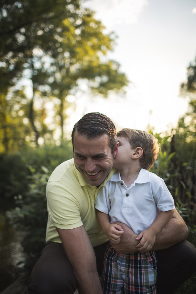 Son kissing father on the cheek surrounded by trees and golden light 