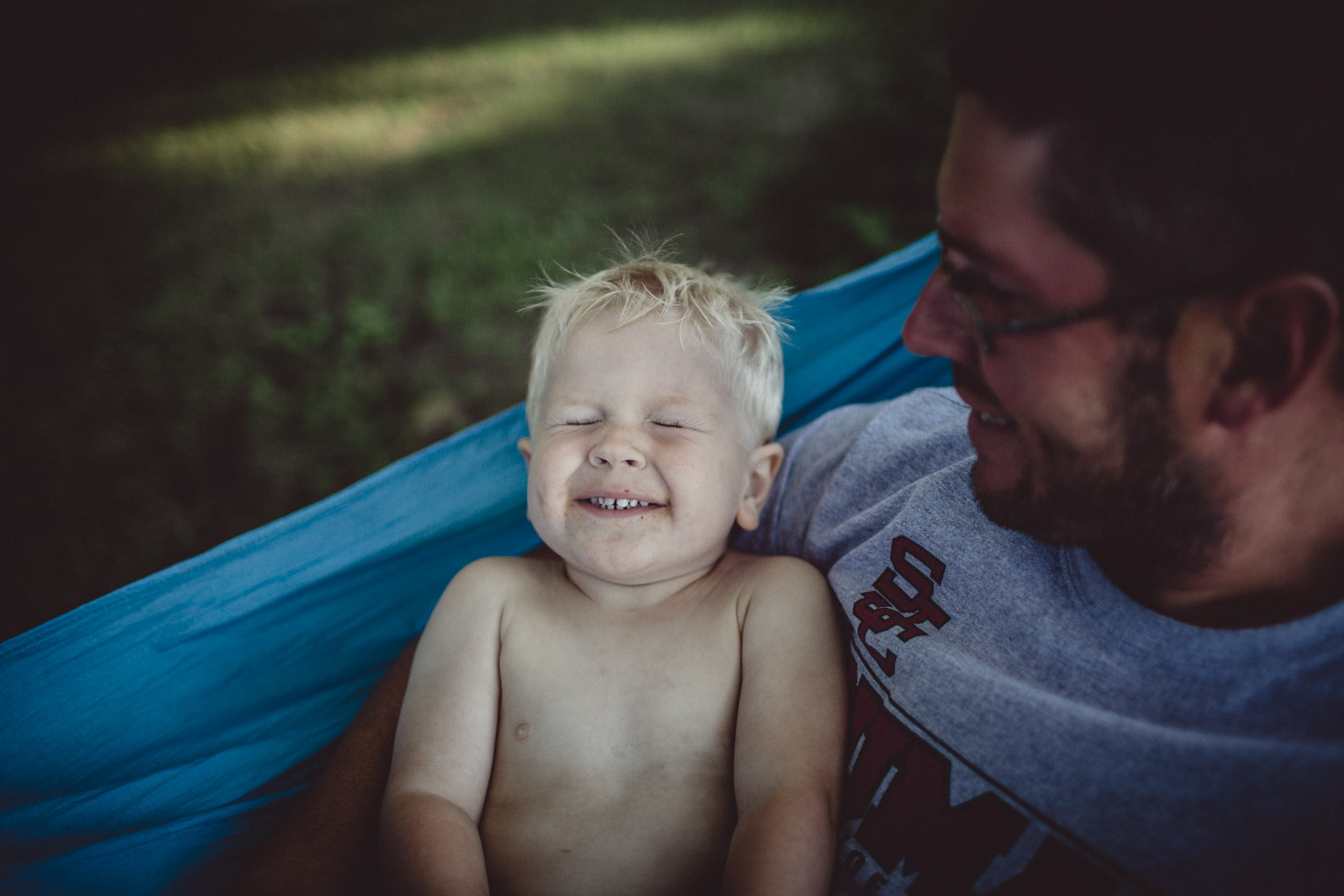 son smiling with joy in fathers arms in hammock, natural light
