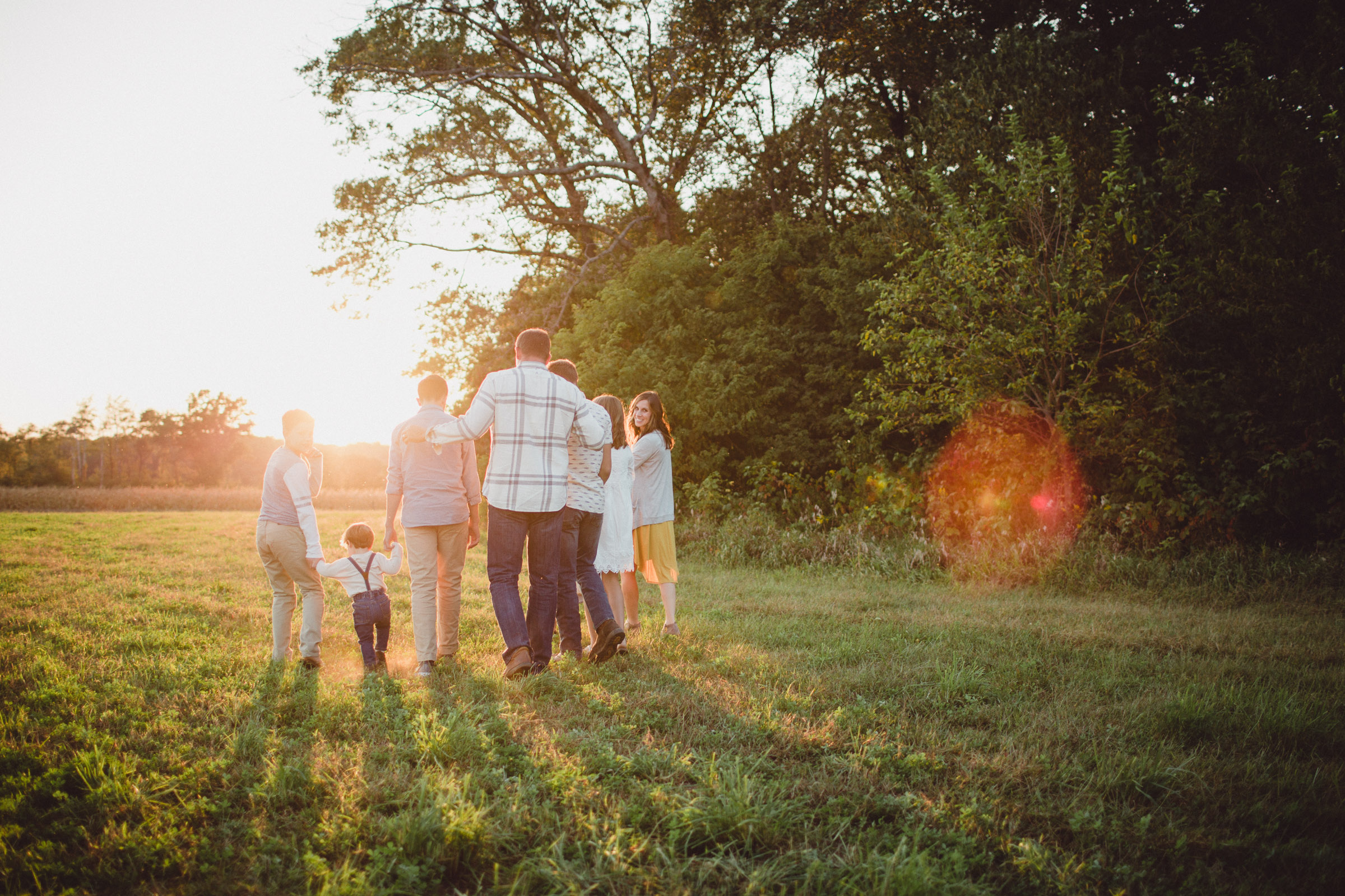 family walking together in field in sun flare 