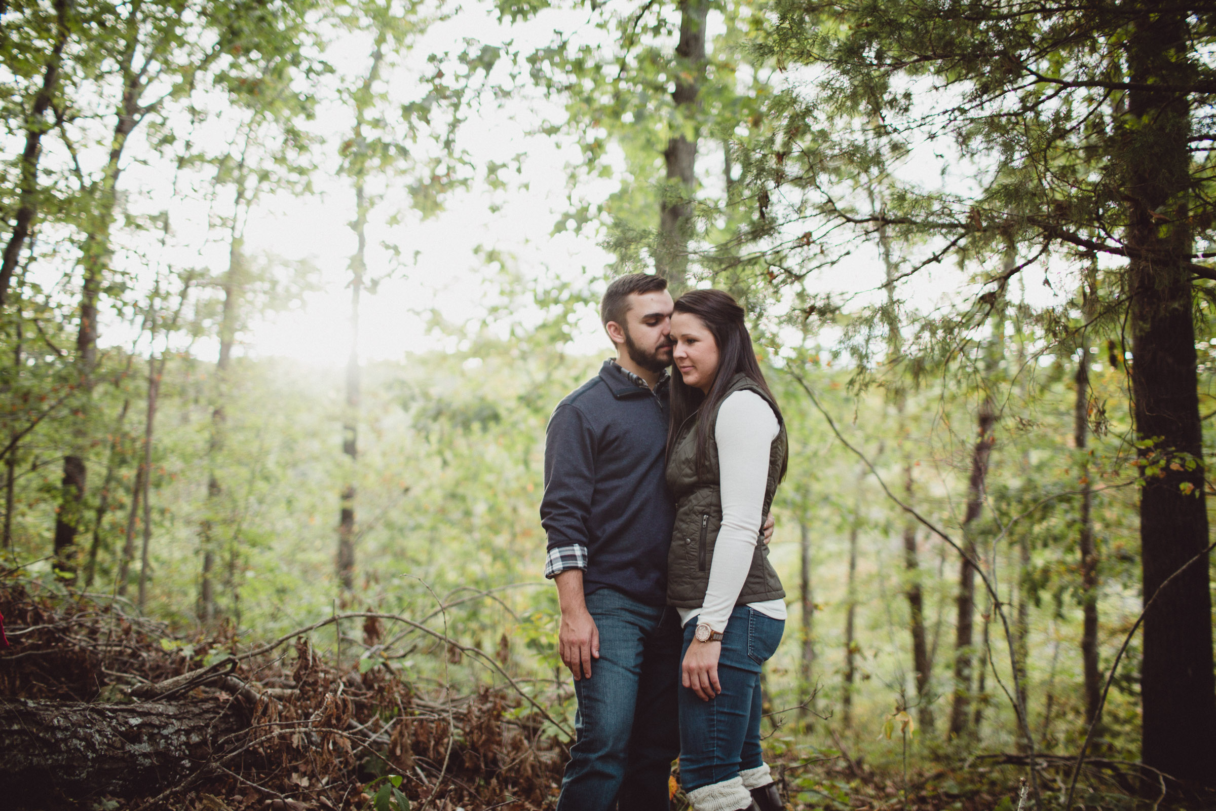 couple snuggling in the midst of large trees 