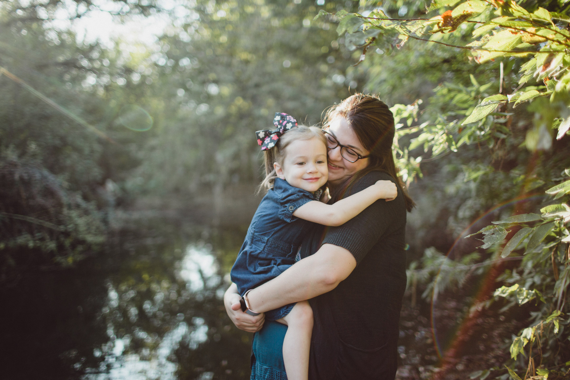 Mother and daughter snuggles in greenery within beautiful light 