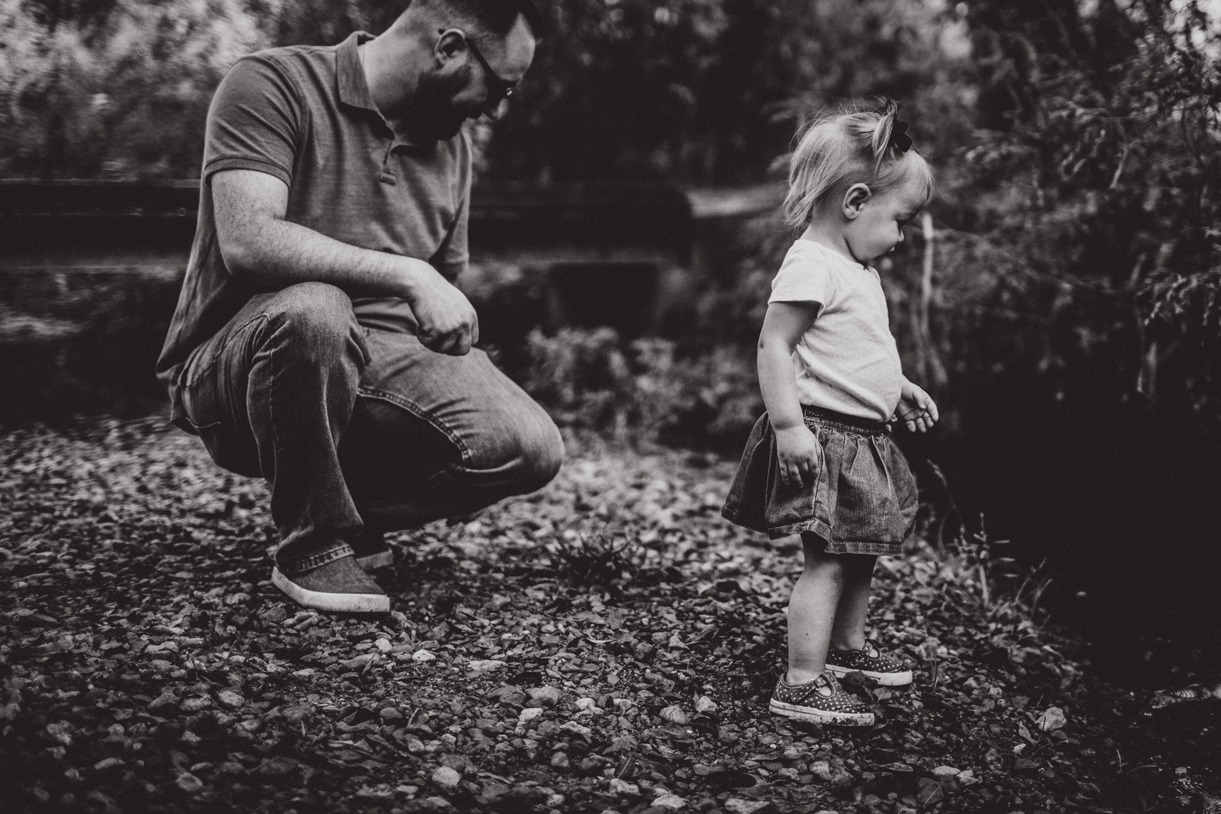 black and white image of father and daughter exploring creek together 