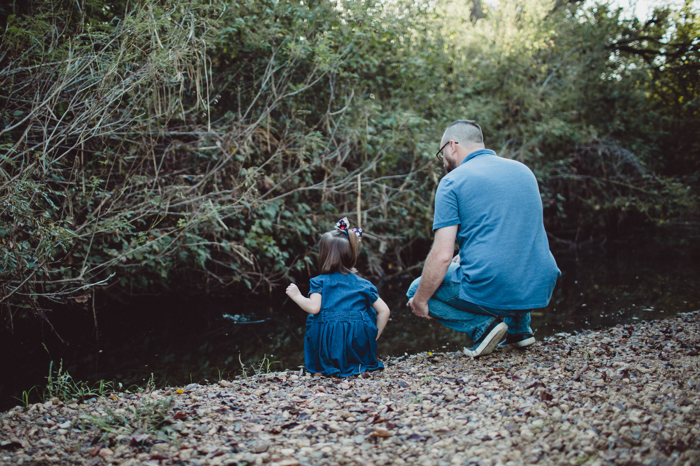 Image of father and daughter throwing rocks into the creek from behind 