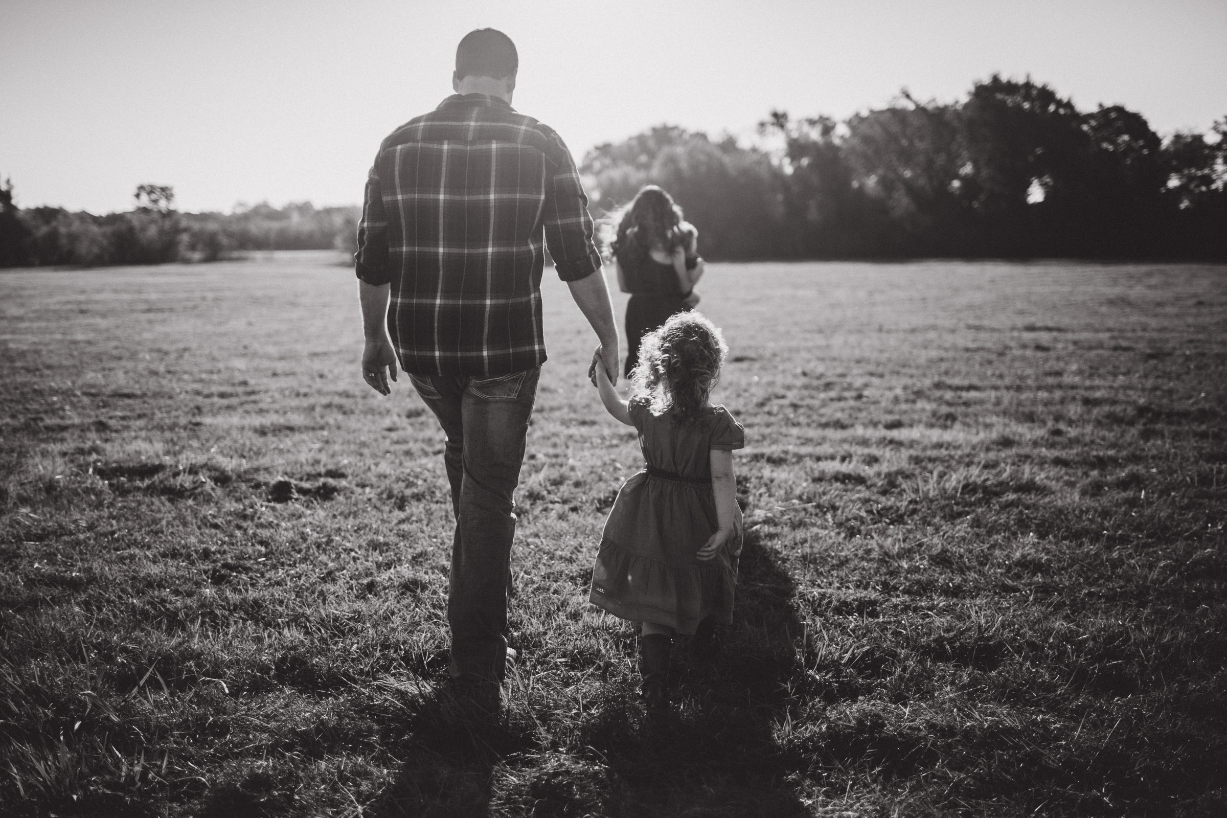 father and daughter walking together into the wind in field hand in hand 