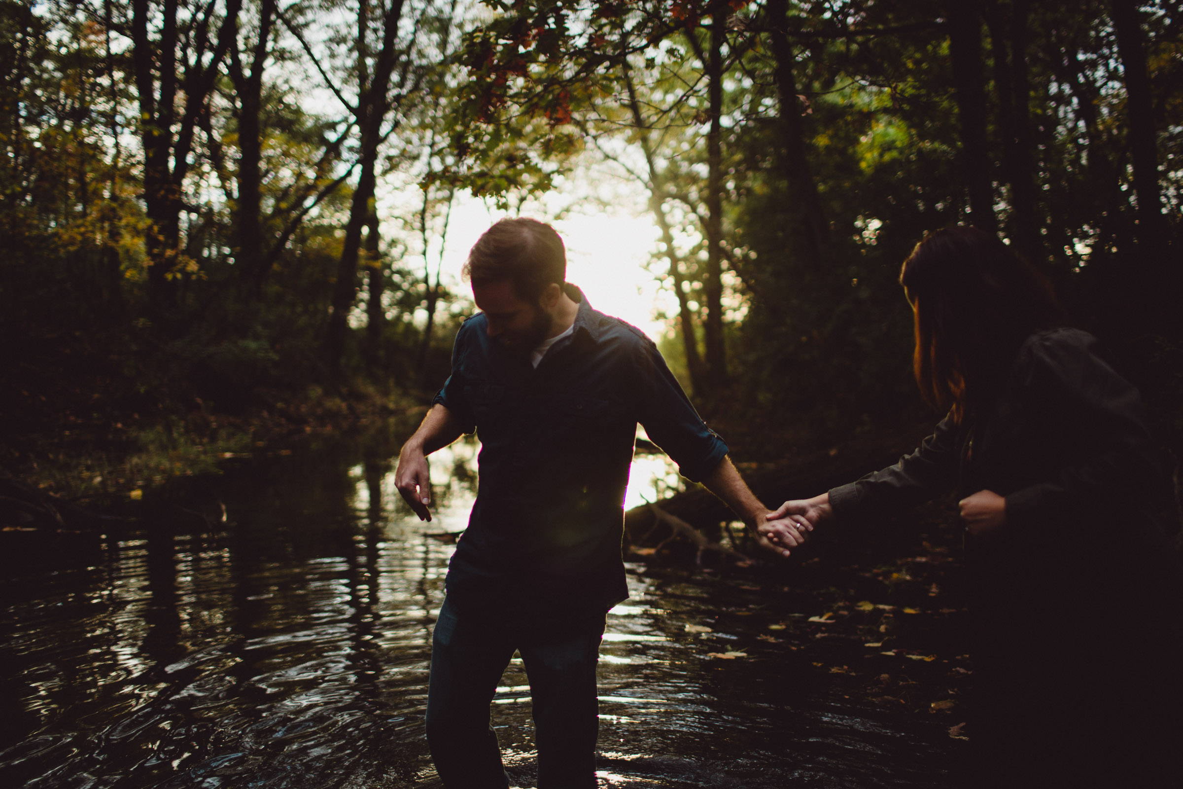 couple walking into beautiful creek with backlight 