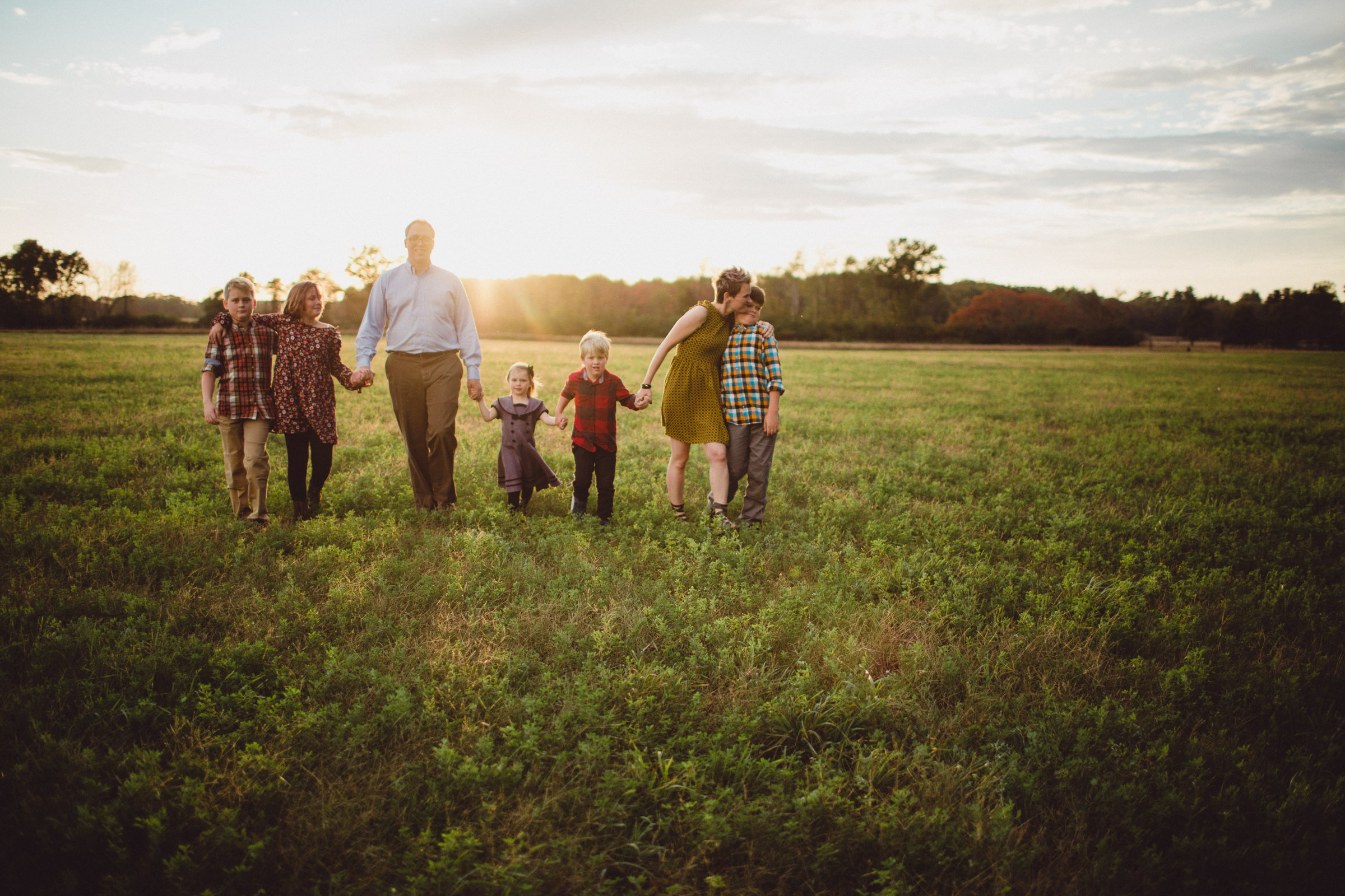 family walking together in wide open field with sun setting behind them 