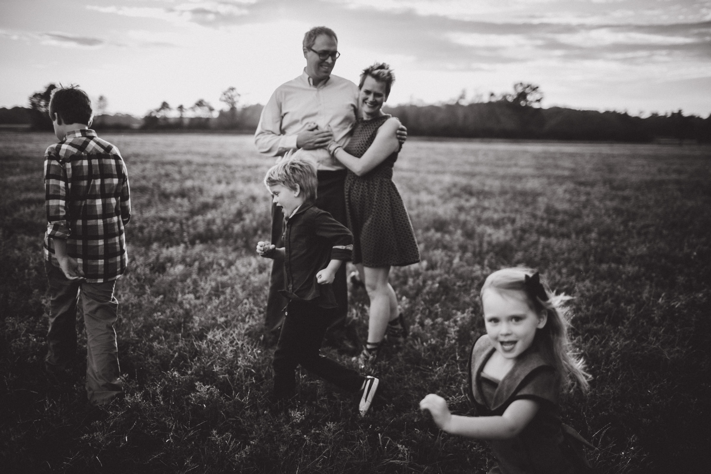 children running around parents in open field, black and white image 