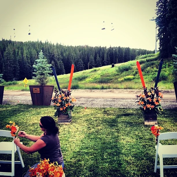 Lauren is putting the aisle decor on the chairs and the ceremony arrangements have orange and navy skis put in them.