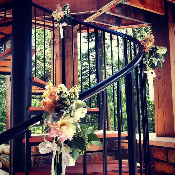 Flowers tied with twine and lace to the spiral staircase that the bride will walk down to the ceremony space. // #wedding #flowers