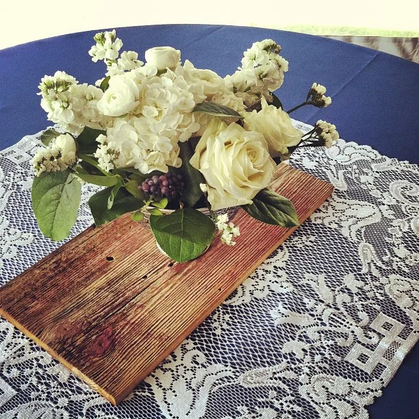 All-white centerpieces on white lace, slabs of wood and blue linen.
