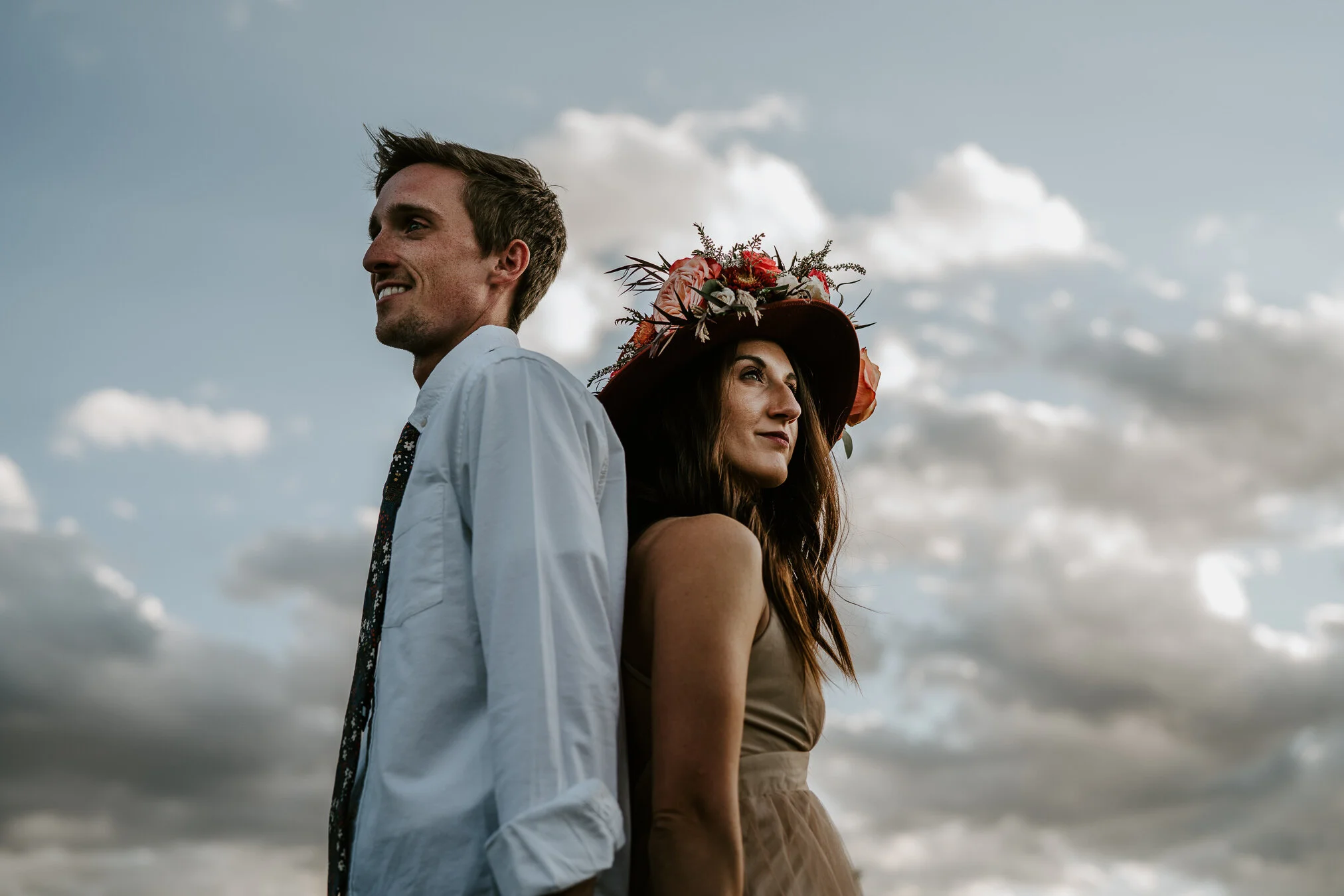 A couple looks in opposite directions with the blue sky behind them.