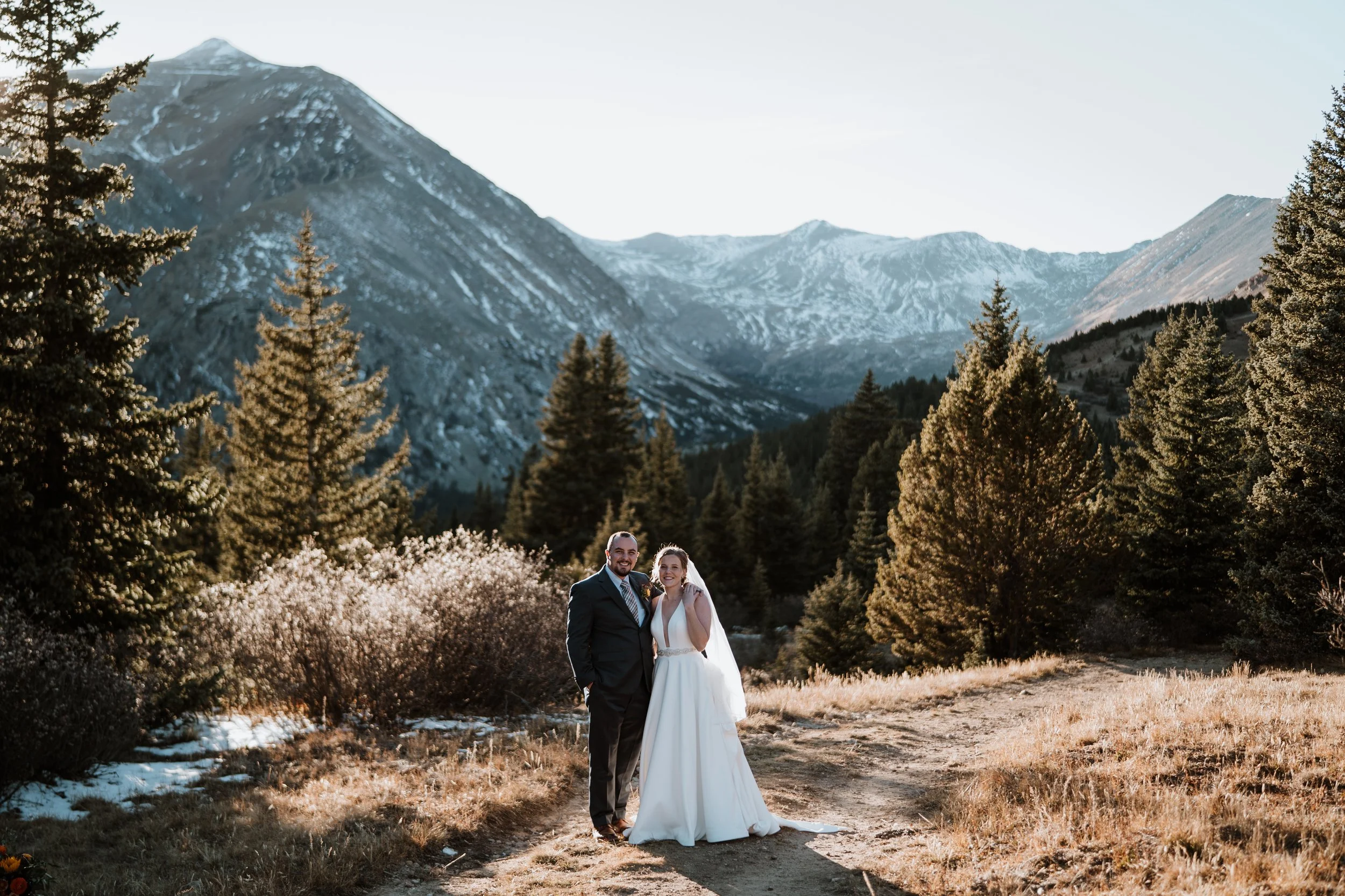 Bride & Groom standing on a trail with towering mountains behind them.