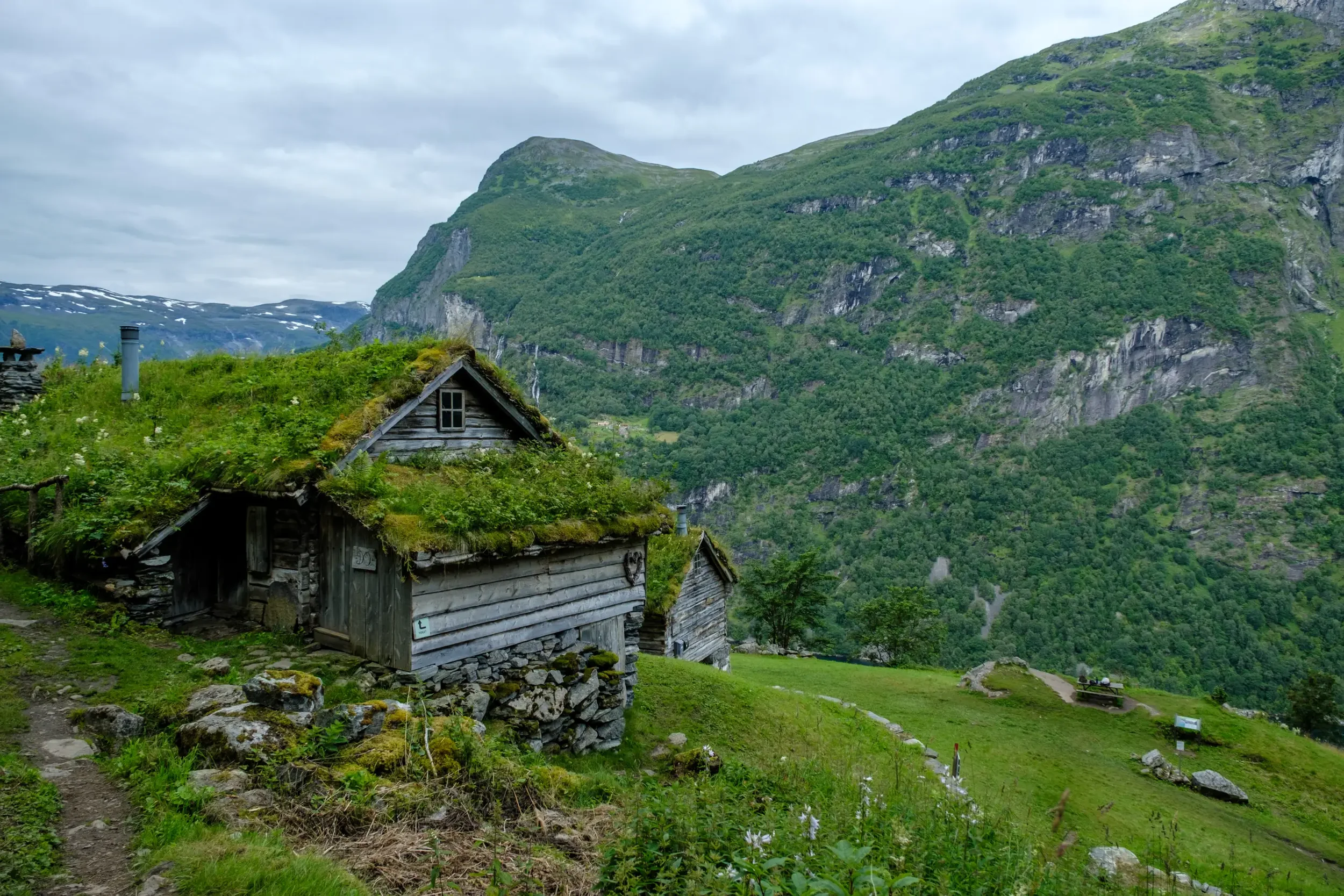 Små tradisjonelle hytter med stråtak i en grønn dal omgitt av høye, grønne fjell.