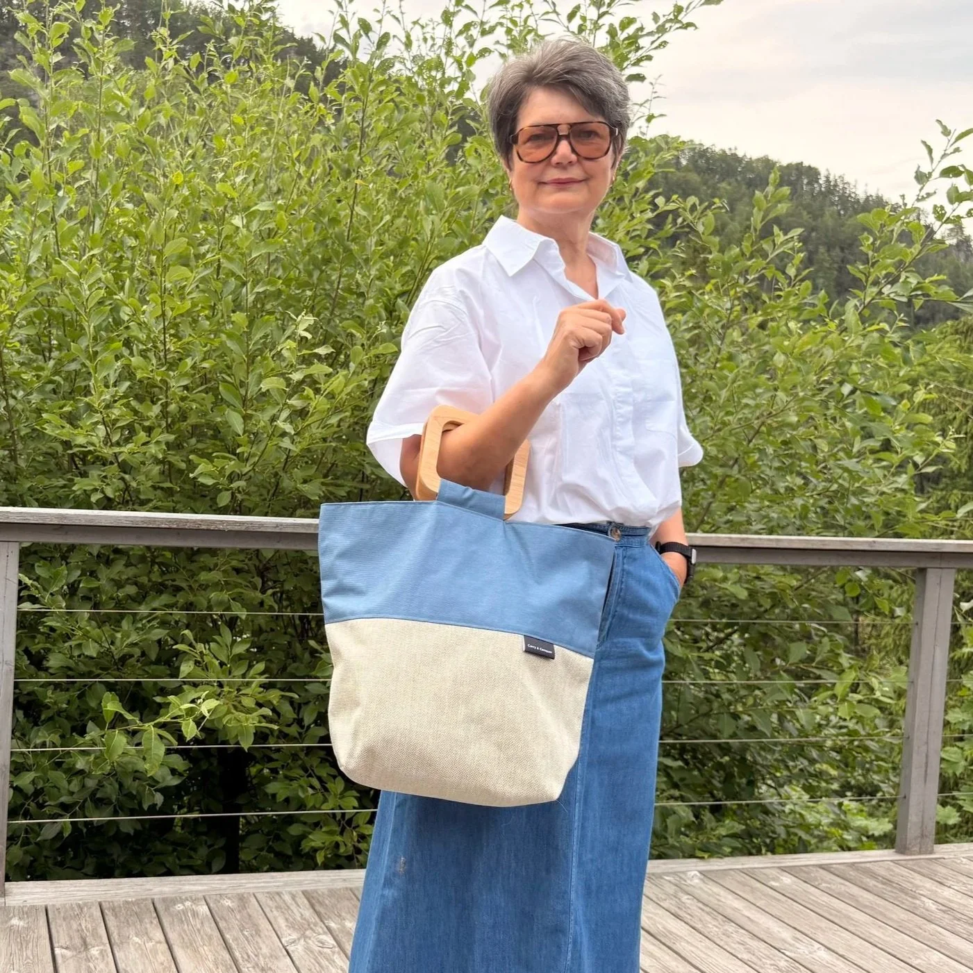 Modell carrying Handmade beige canvas tote bag with dusty blue accents and geometric square wooden handles - on her arm.