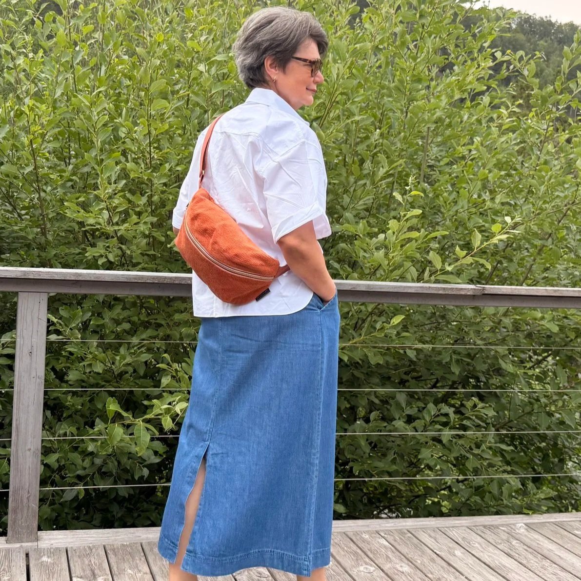 Model wearing an adjustable burnt orange corduroy sling bag across the chest for hands-free travel.
