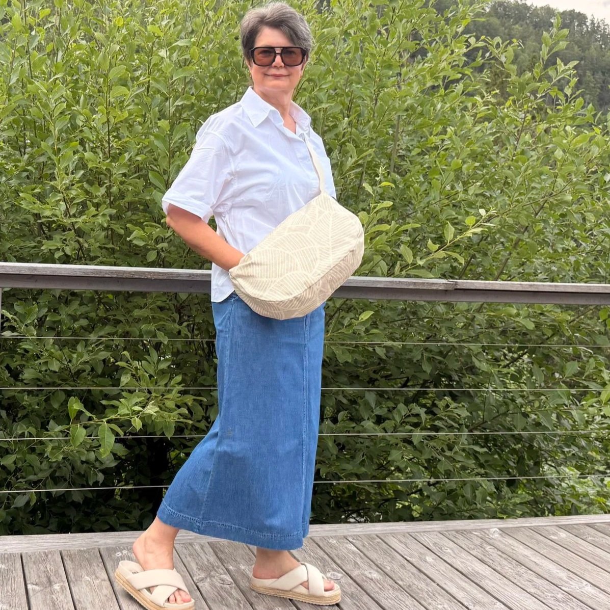 Model wearing an ergonomic sand-beige moon bag as a high-chest sling to show fit.