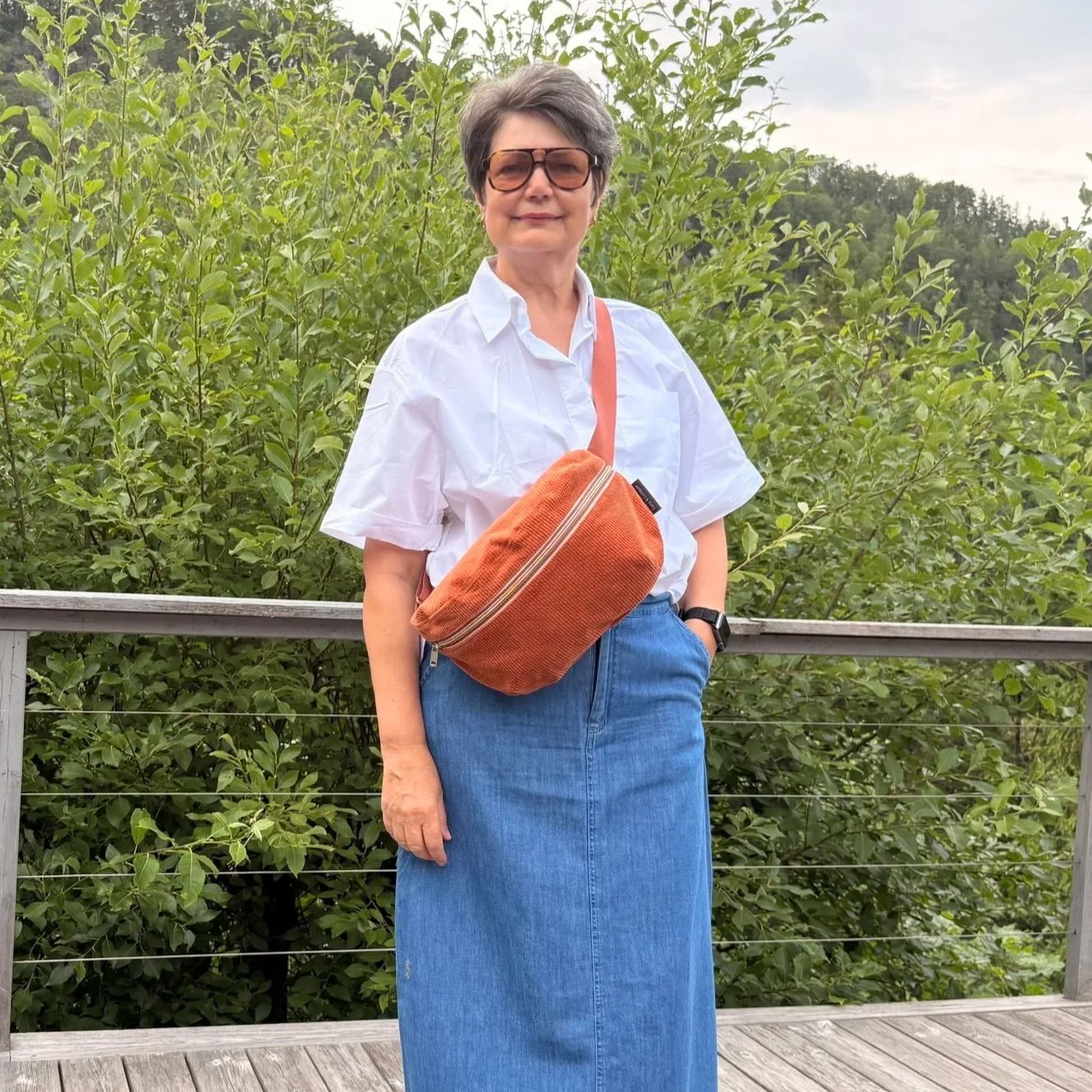 Model wearing an adjustable burnt orange corduroy sling bag across the chest for hands-free travel.