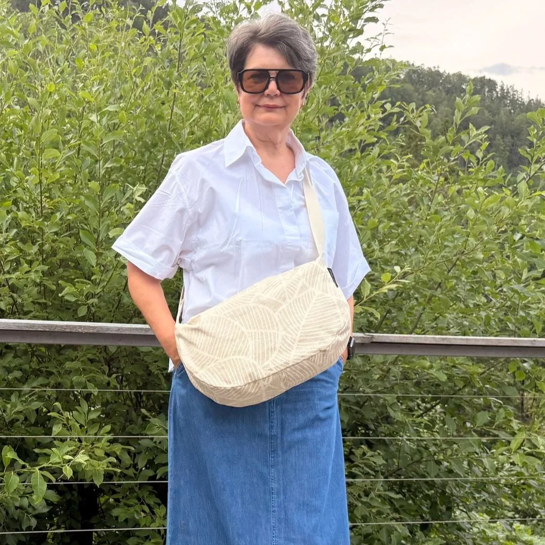 Model wearing an ergonomic sand-beige moon bag as a high-chest sling to show fit.
