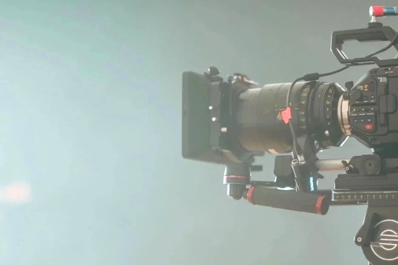 Camera with a large telephoto lens mounted on a tripod, pointed toward the sky, with a light gray background.