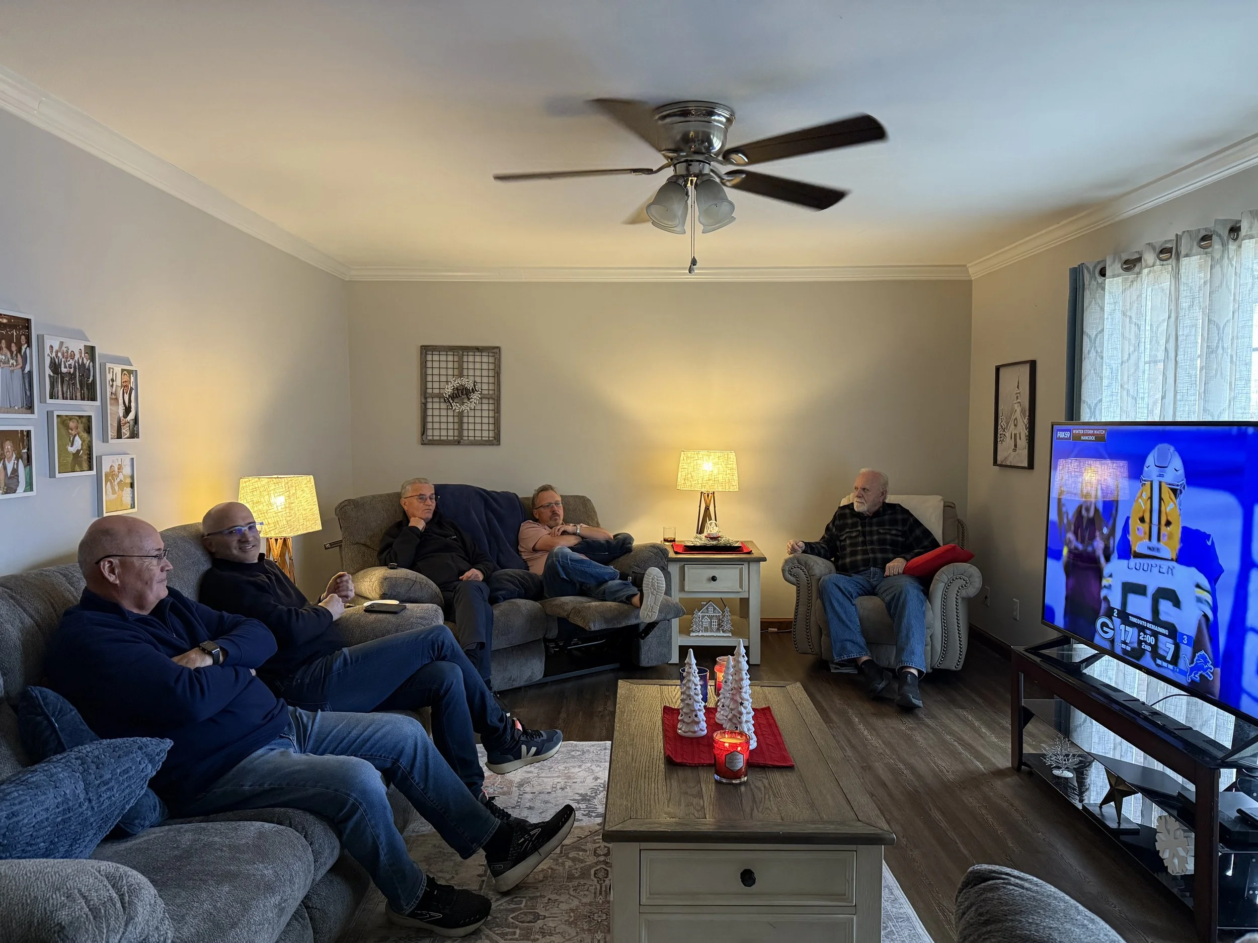 Men seated on sofas and chairs watching a football game in a cozy living room.