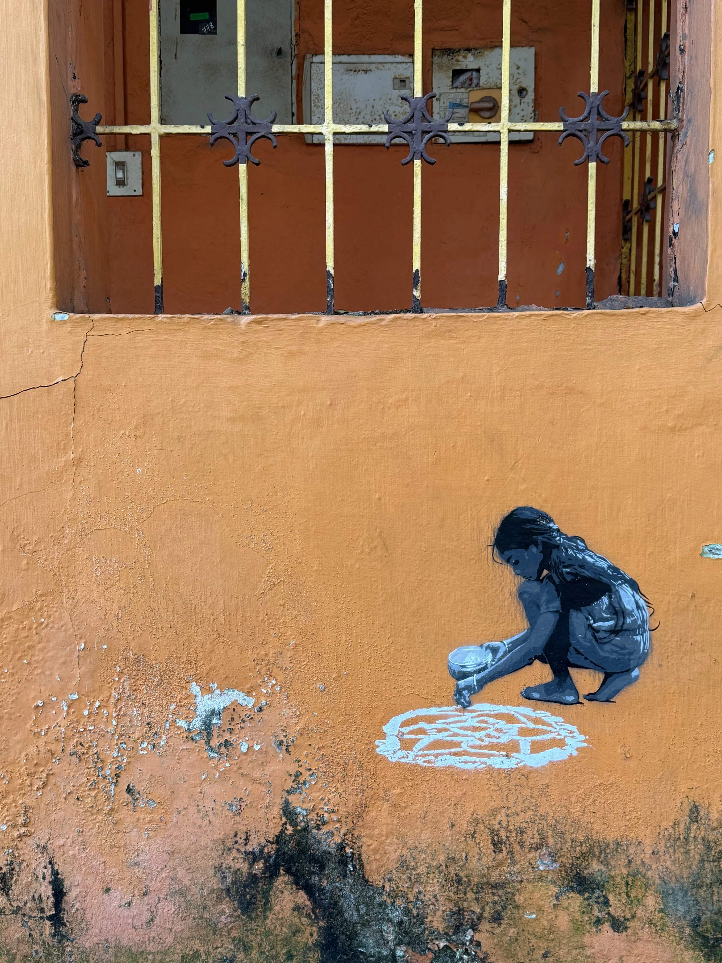 Street art of a child painting a white circle on an orange wall.