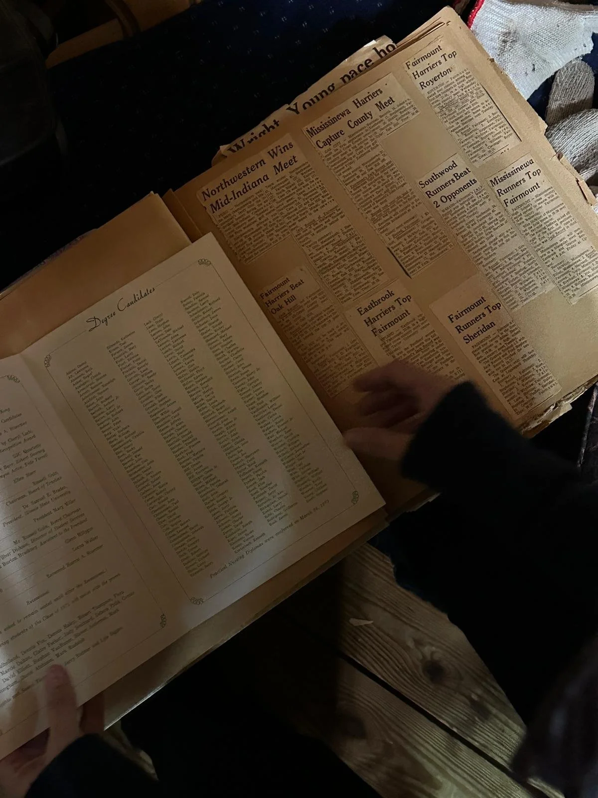 Hands turning pages of an old album filled with newspaper clippings.