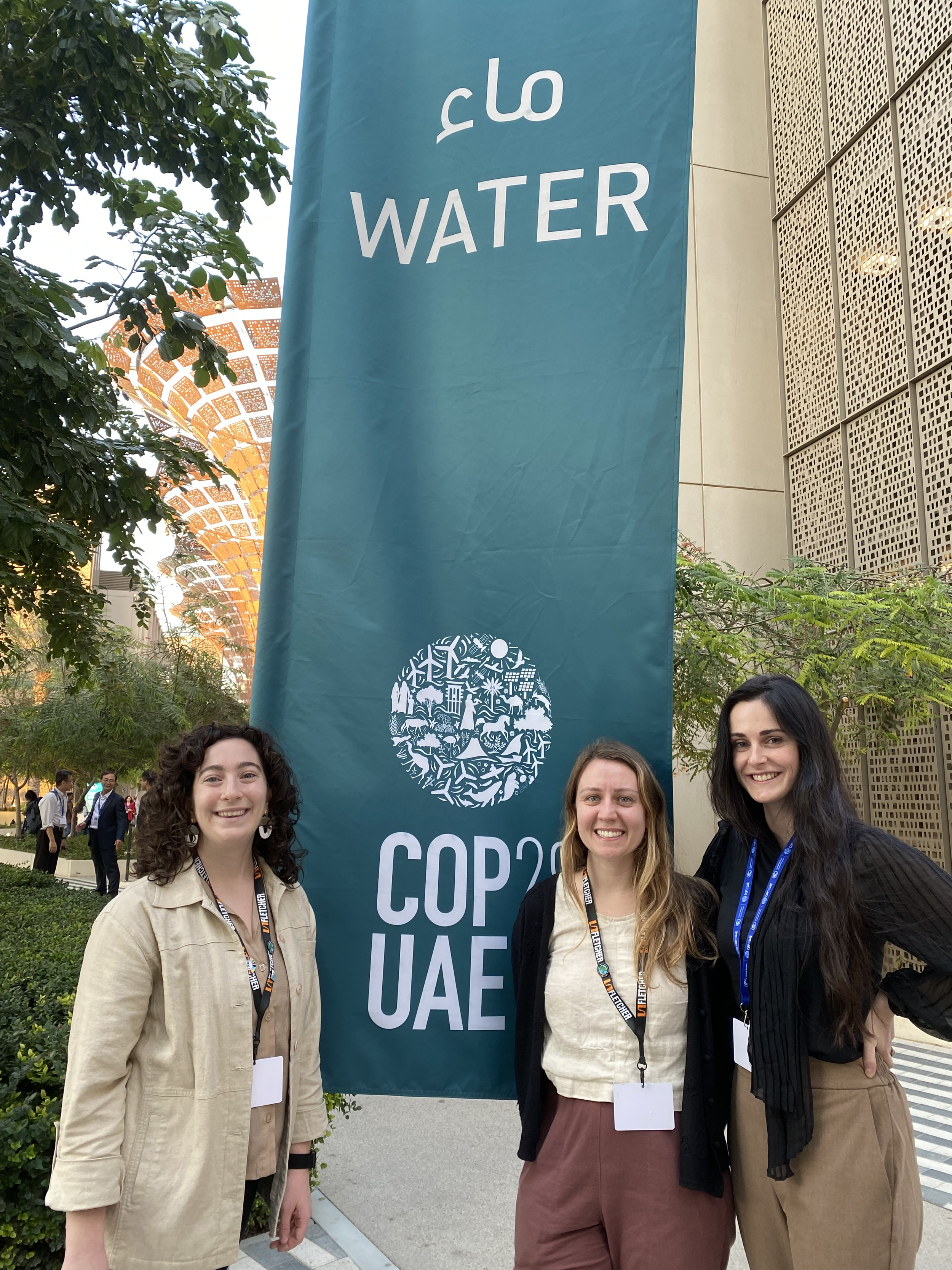 Alyssa, Selena, and Alexandra in front of the water sign at COP28.png