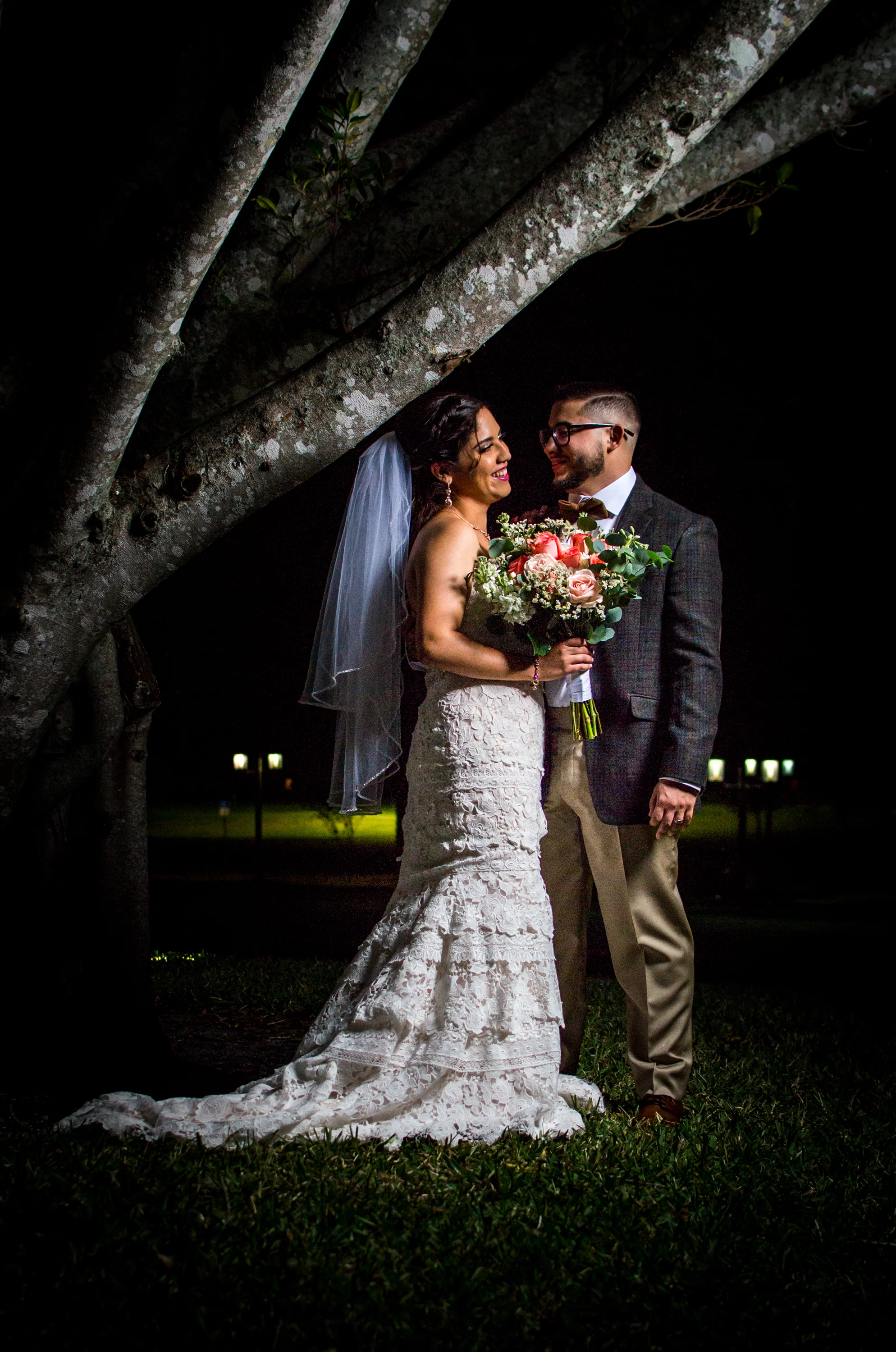 Bride and groom smiling under a tree at night.